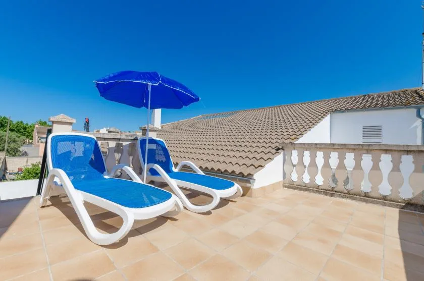 A sunny rooftop terrace has blue lounge seating beneath an umbrella.