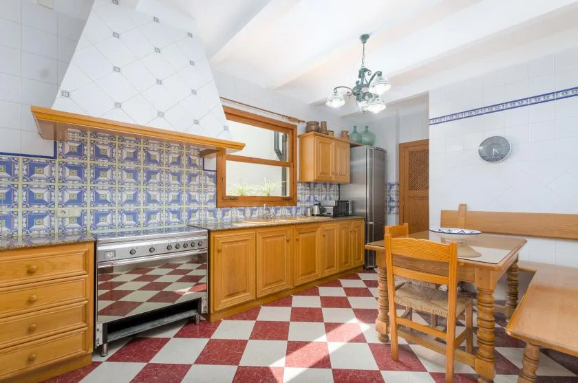 A tiled kitchen with wooden cabinets, a large range, and a dining table.