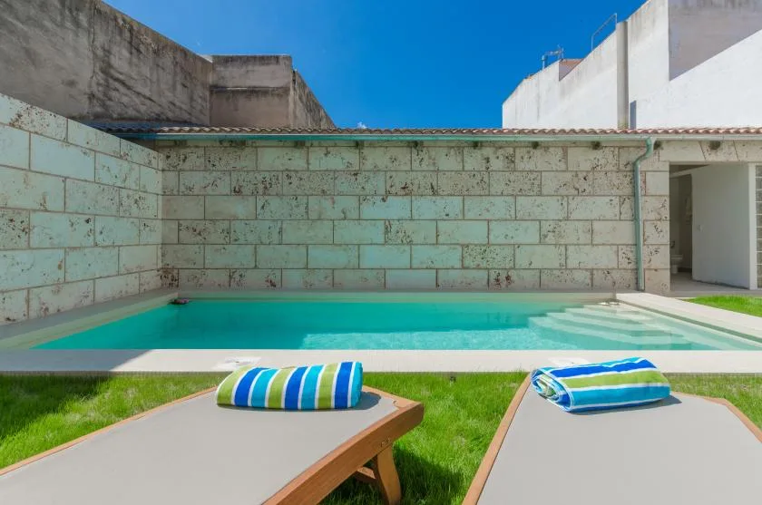 A swimming pool beside a grassy patio with two sun loungers.