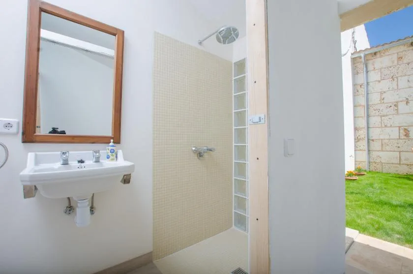A bathroom with a wall-mounted sink and an open shower area beside a garden.