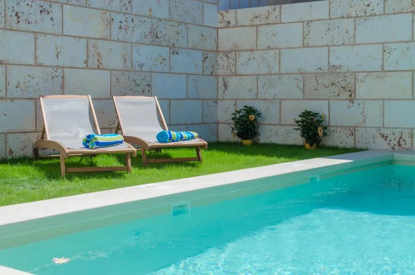 An outdoor swimming pool borders a grassy area with two lounge chairs.