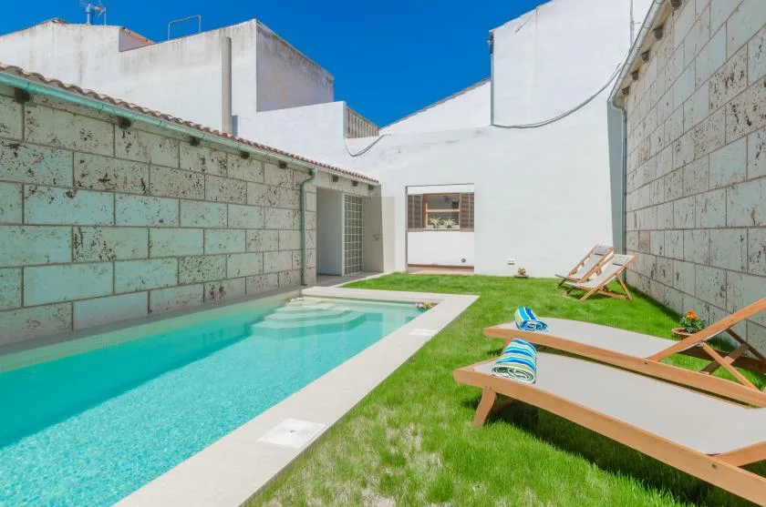 A small outdoor pool beside a grassy courtyard with wooden loungers.