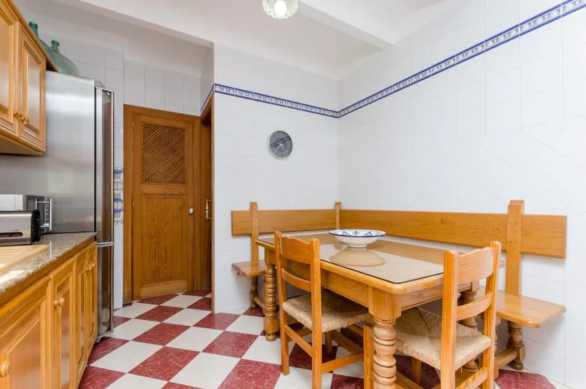 A tiled dining area with a wooden table and chairs beside kitchen cabinets.