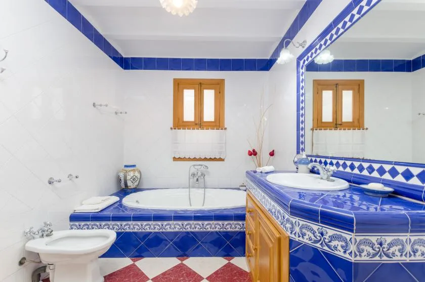 A bathroom with a bathtub and a blue-tiled vanity beside a large mirror.