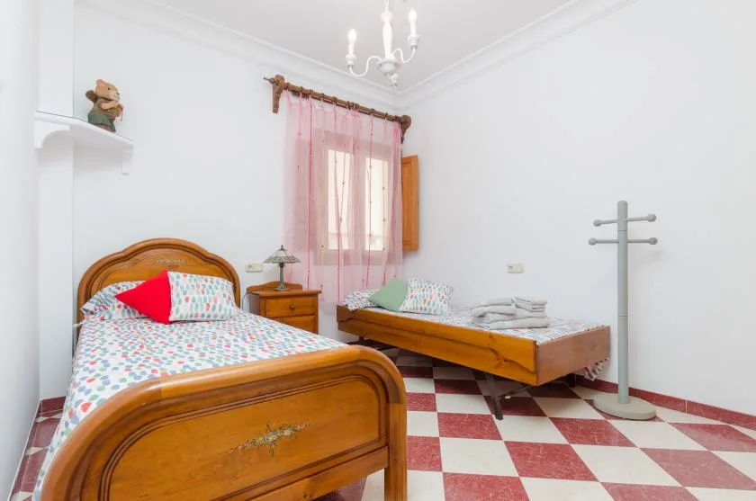 A bedroom with two wooden beds, patterned bedding, and a pink-curtained window.