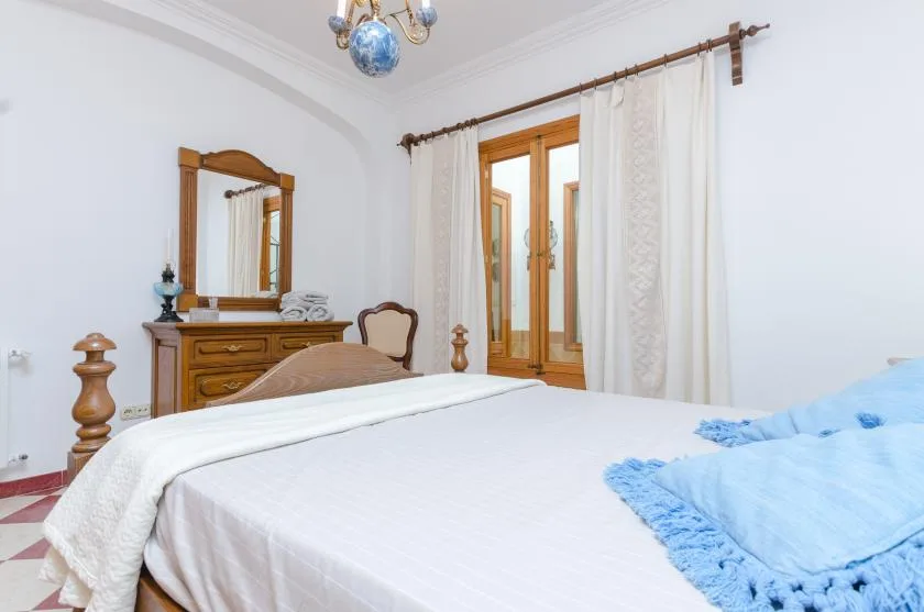 A bedroom with a neatly made bed and wooden-framed windows.