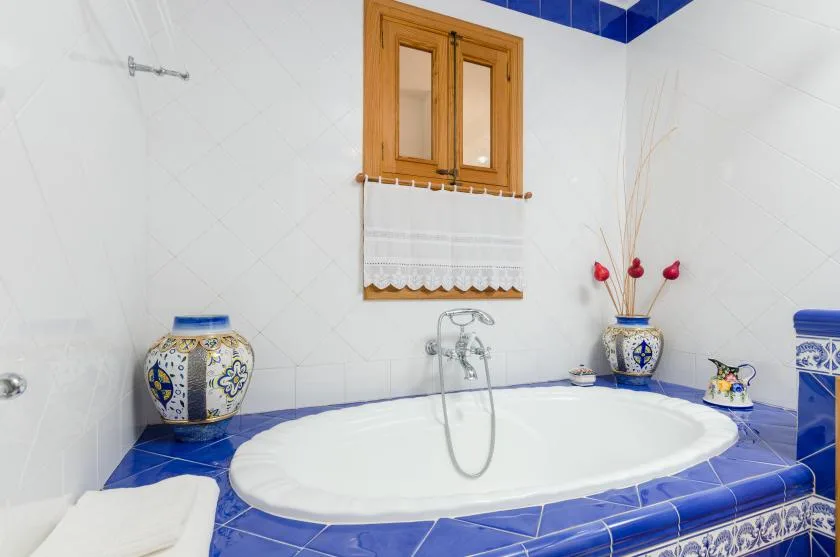 A tiled bathroom features a large bathtub beneath a small window.