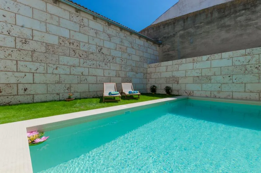 An outdoor swimming pool beside a narrow strip of lawn and two lounge chairs.