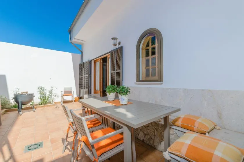 An outdoor dining area with a table and orange-cushioned seating beside a white wall.