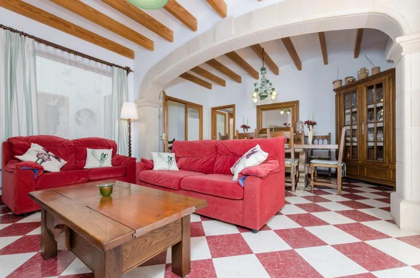 A living room with red seating and a wooden coffee table beneath exposed ceiling beams.