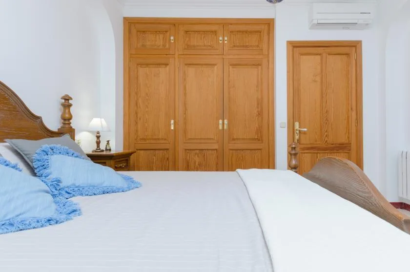 A bedroom with a large bed, wooden wardrobes, and a matching wooden door.
