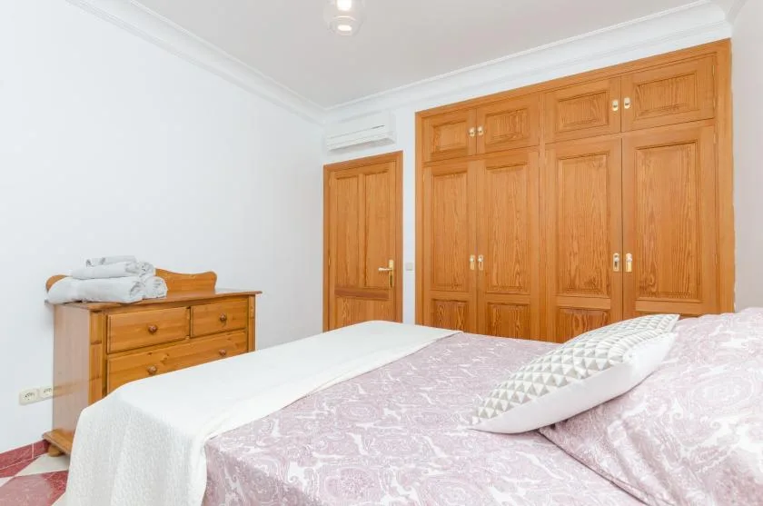 A bedroom with a bed covered in pale patterned bedding and wooden wardrobes.