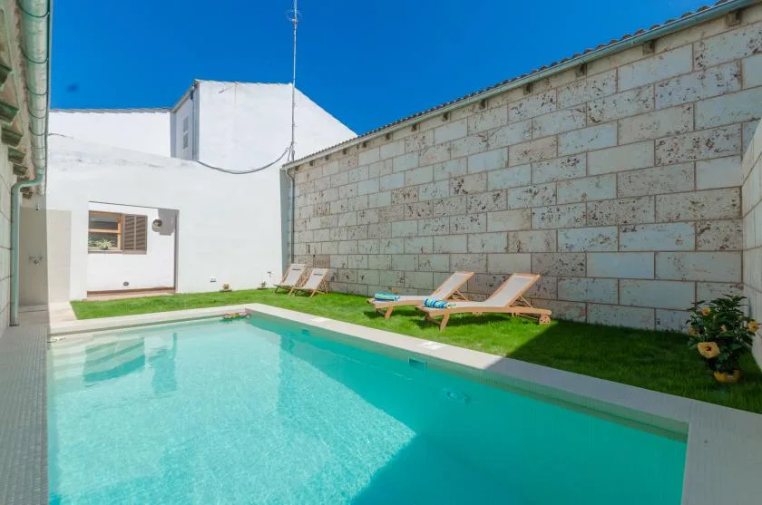 A swimming pool beside a grassy patio with lounge chairs.