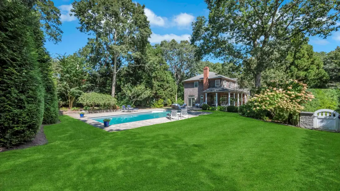 Un patio ajardinado cuenta con una piscina y una casa rodeadas de árboles.
