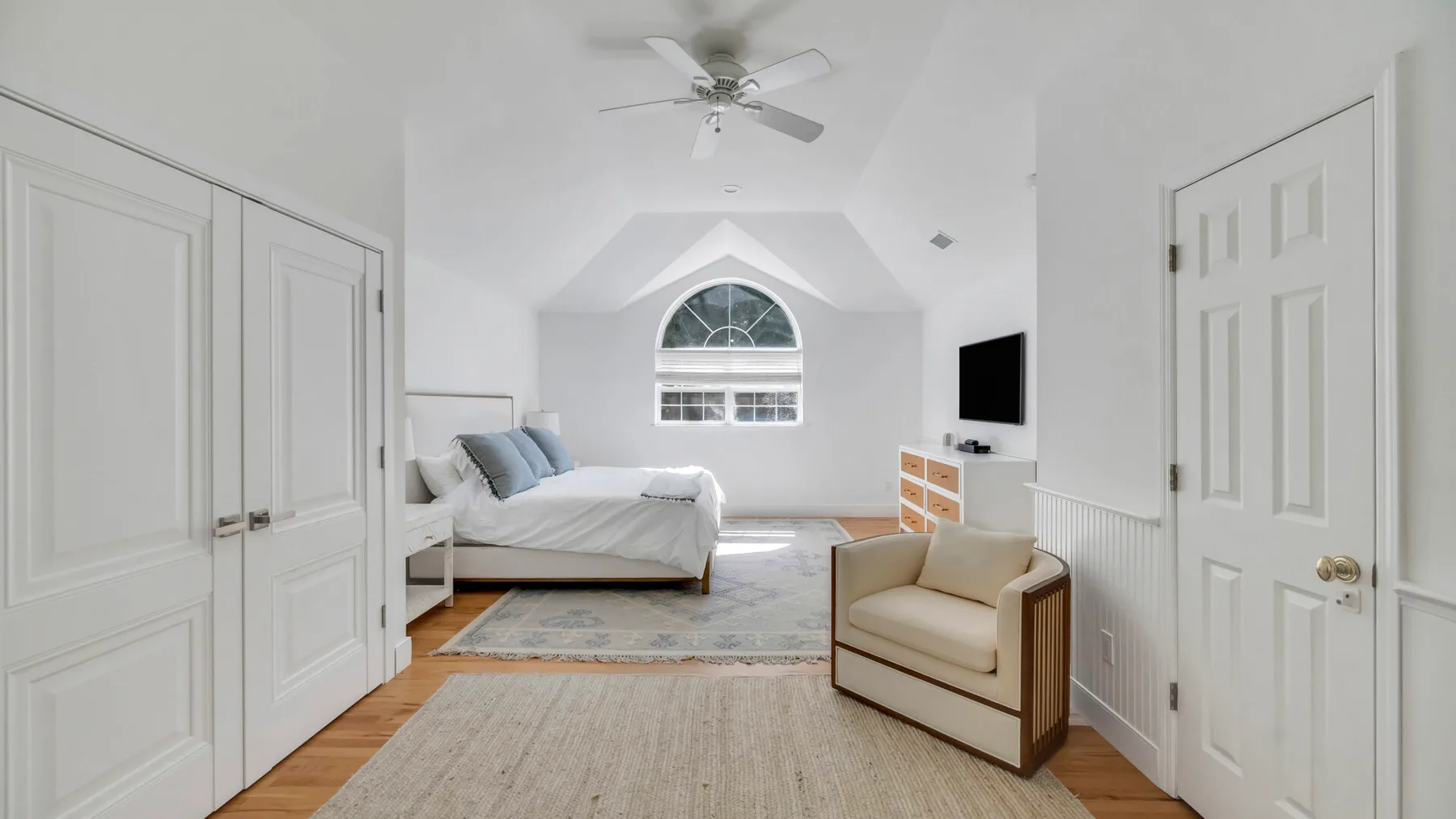 Un dormitorio luminoso con cama, asiento y una ventana bajo un techo abovedado.