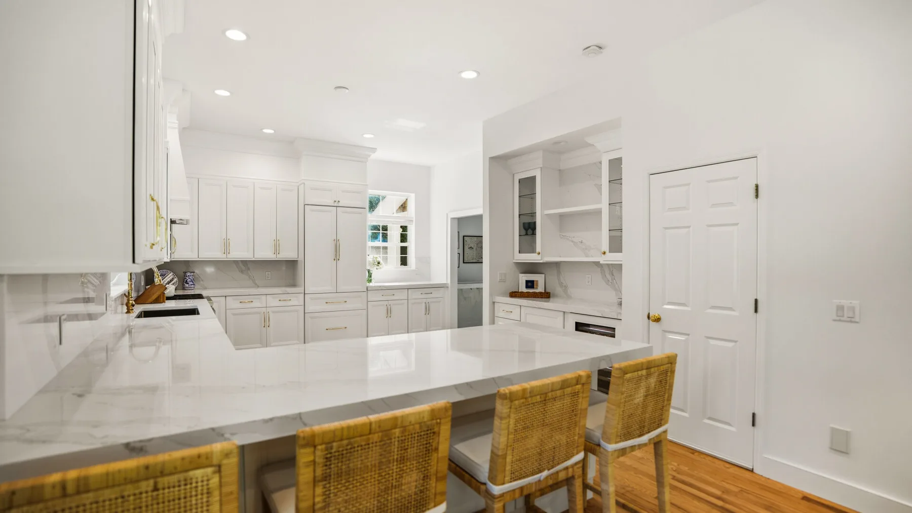 Una cocina luminosa con gabinetes blancos, una isla grande y asientos tejidos.