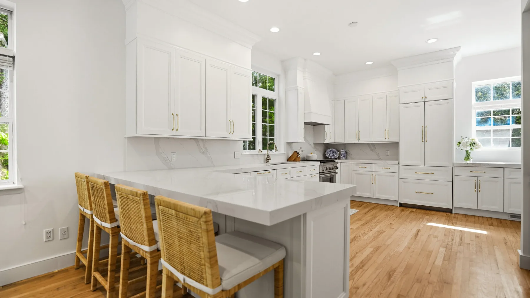 Una cocina blanca y luminosa con una isla central y asientos de mimbre.
