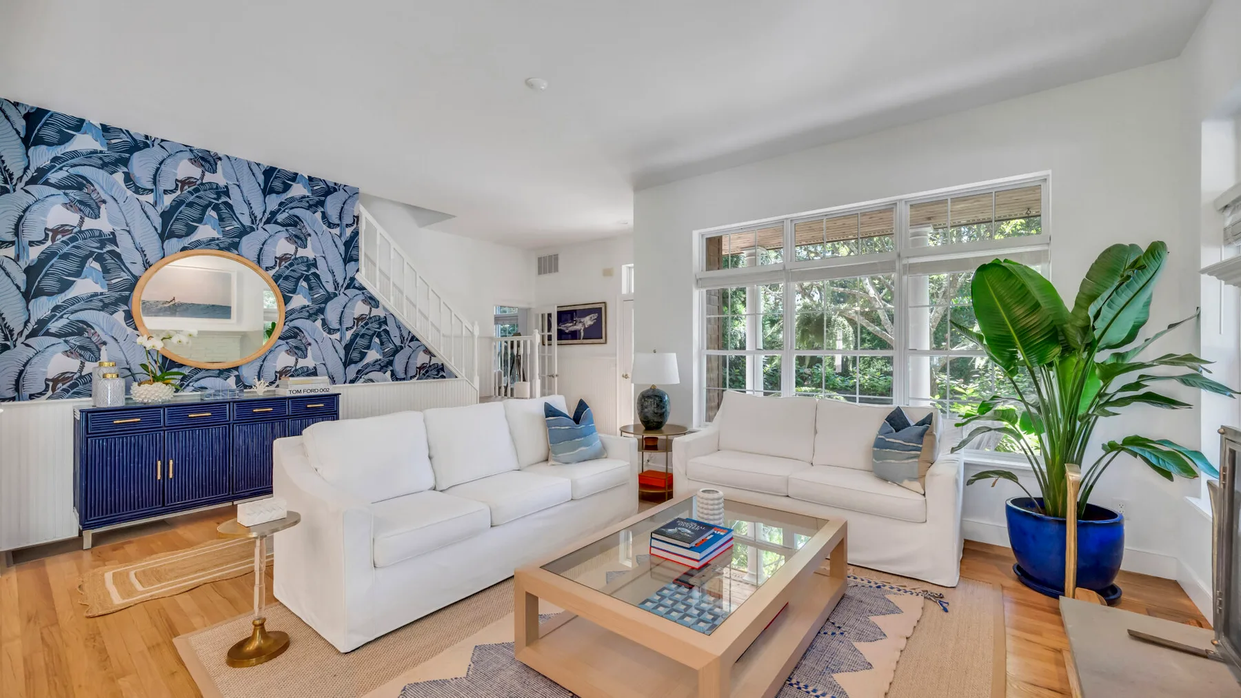 Una sala luminosa con asientos blancos, una mesa de centro de cristal y ventanas grandes.