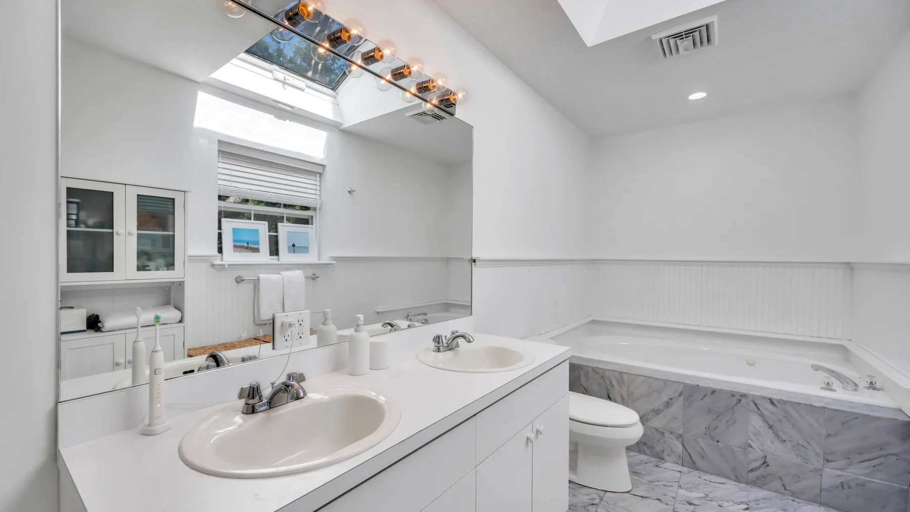 Un baño luminoso cuenta con un tocador de dos lavabos y una bañera.