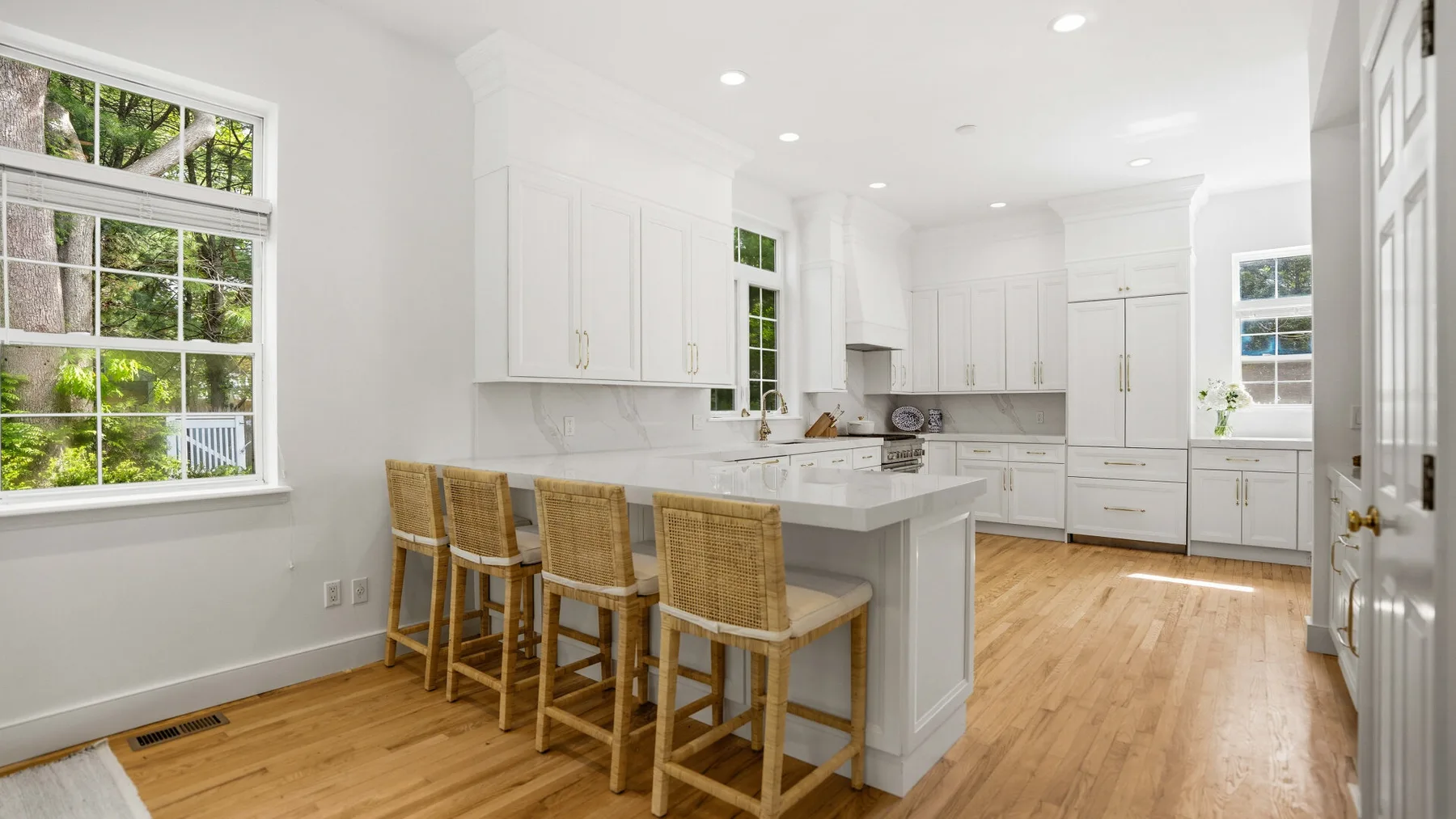 Una cocina luminosa con gabinetes blancos, una isla central y piso de madera.