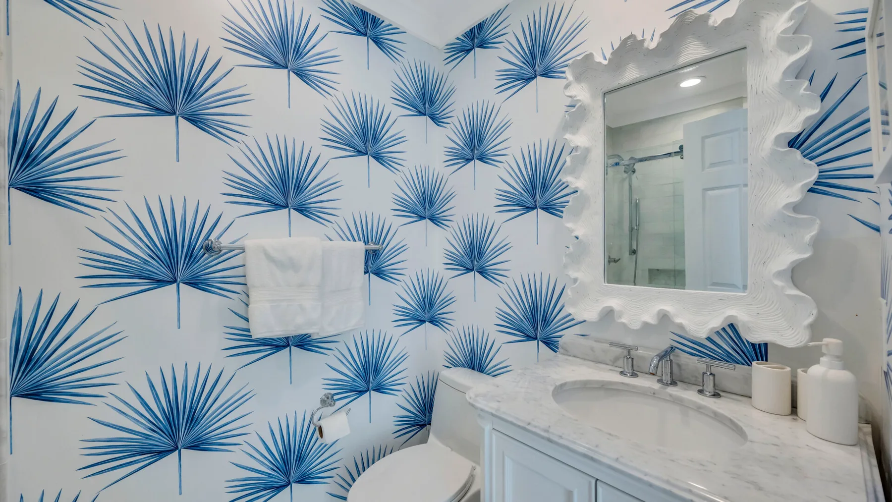 Un tocador y un espejo de baño están frente a un papel tapiz con palmeras azules.