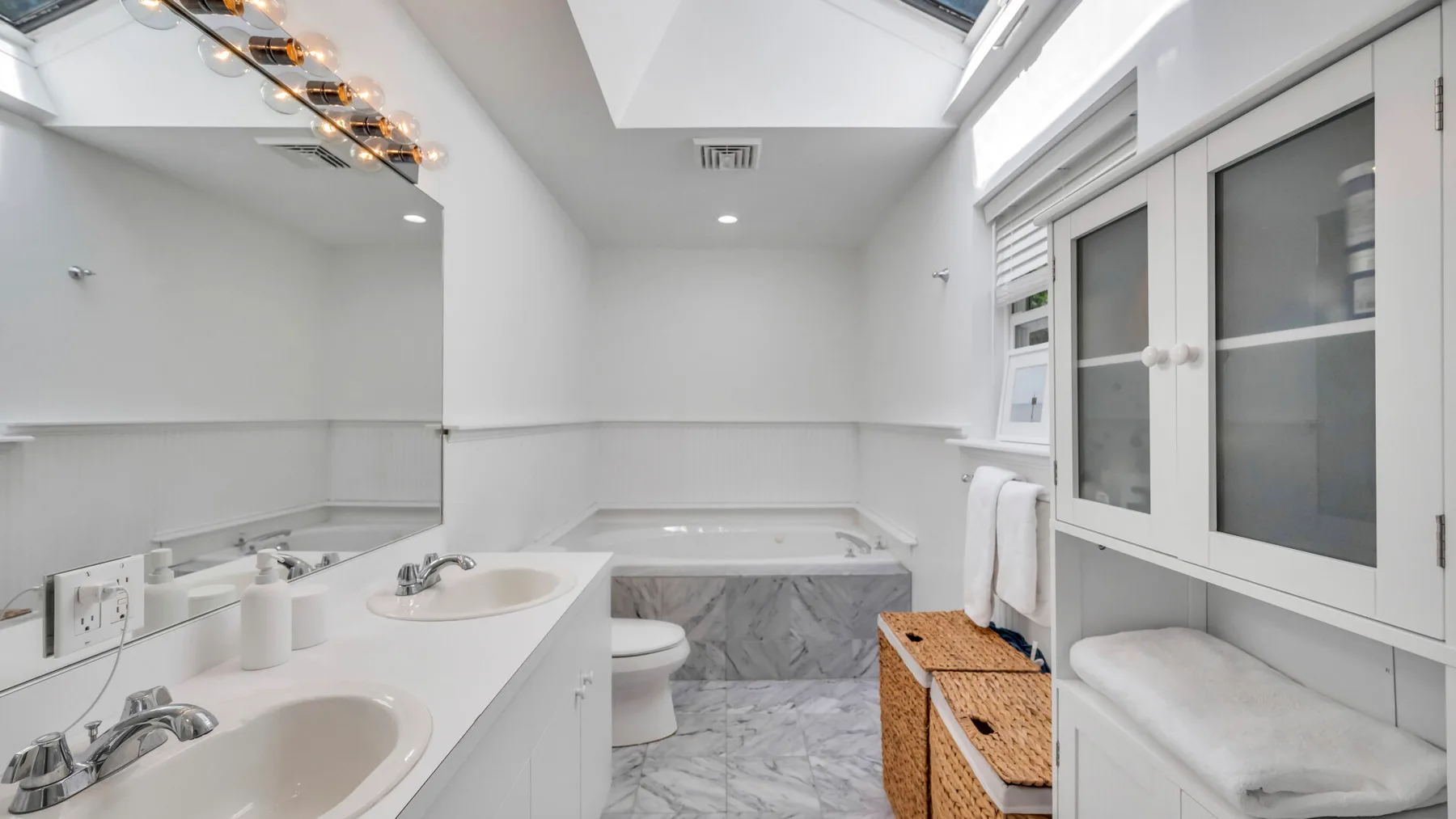 Un baño luminoso con un espejo grande, bañera y asiento junto a la ventana.