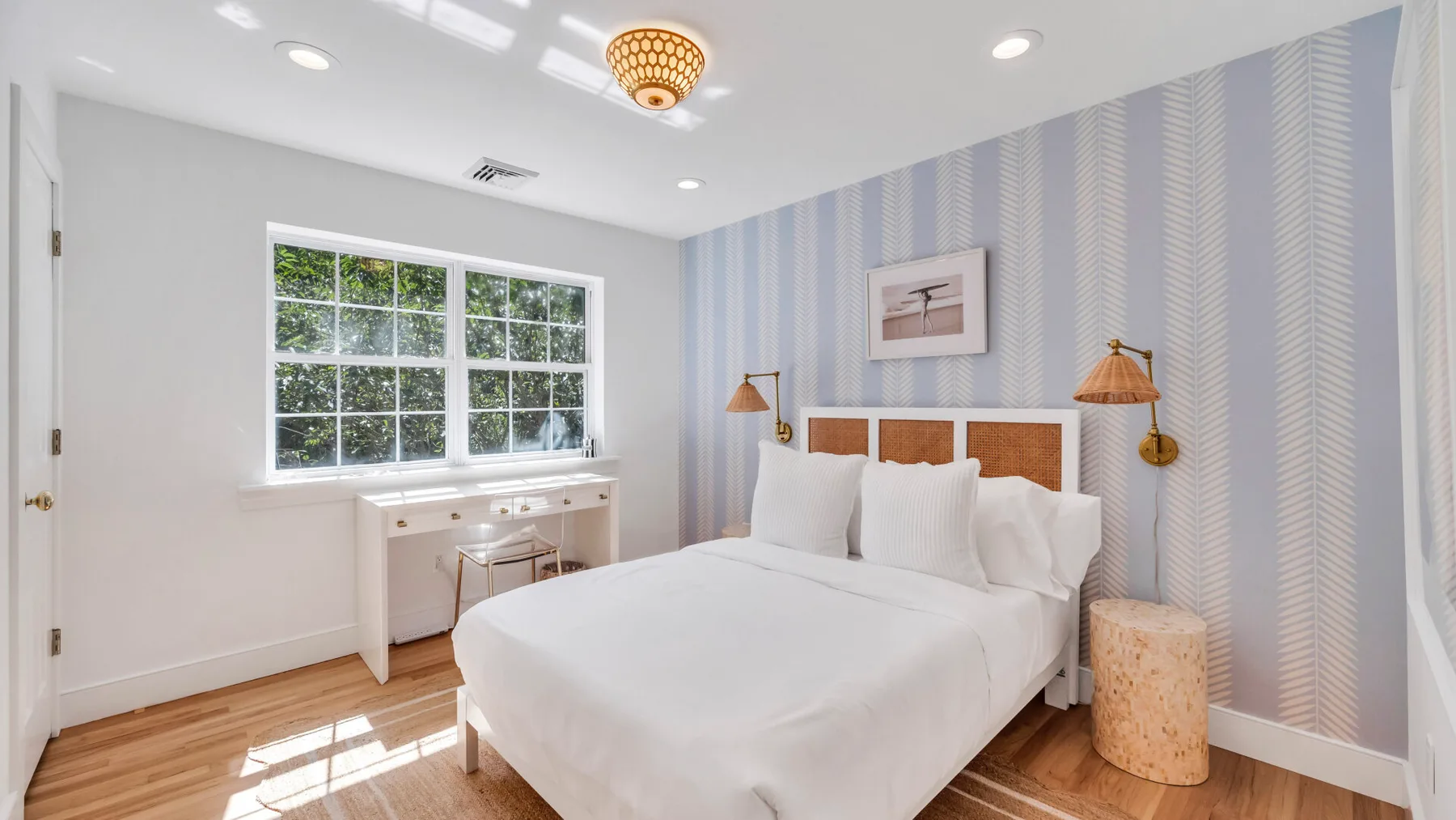 Un dormitorio luminoso con una cama blanca, paredes a rayas y una ventana grande.