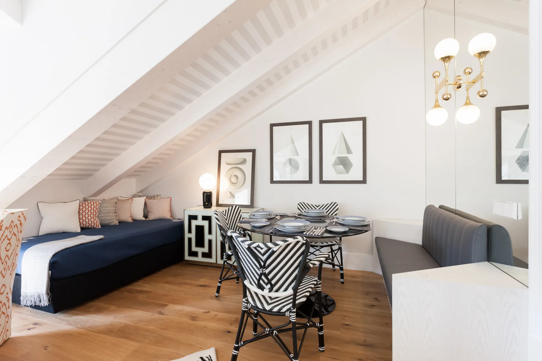 Un comedor con la mesa puesta está junto a una zona de estar bajo un techo inclinado.