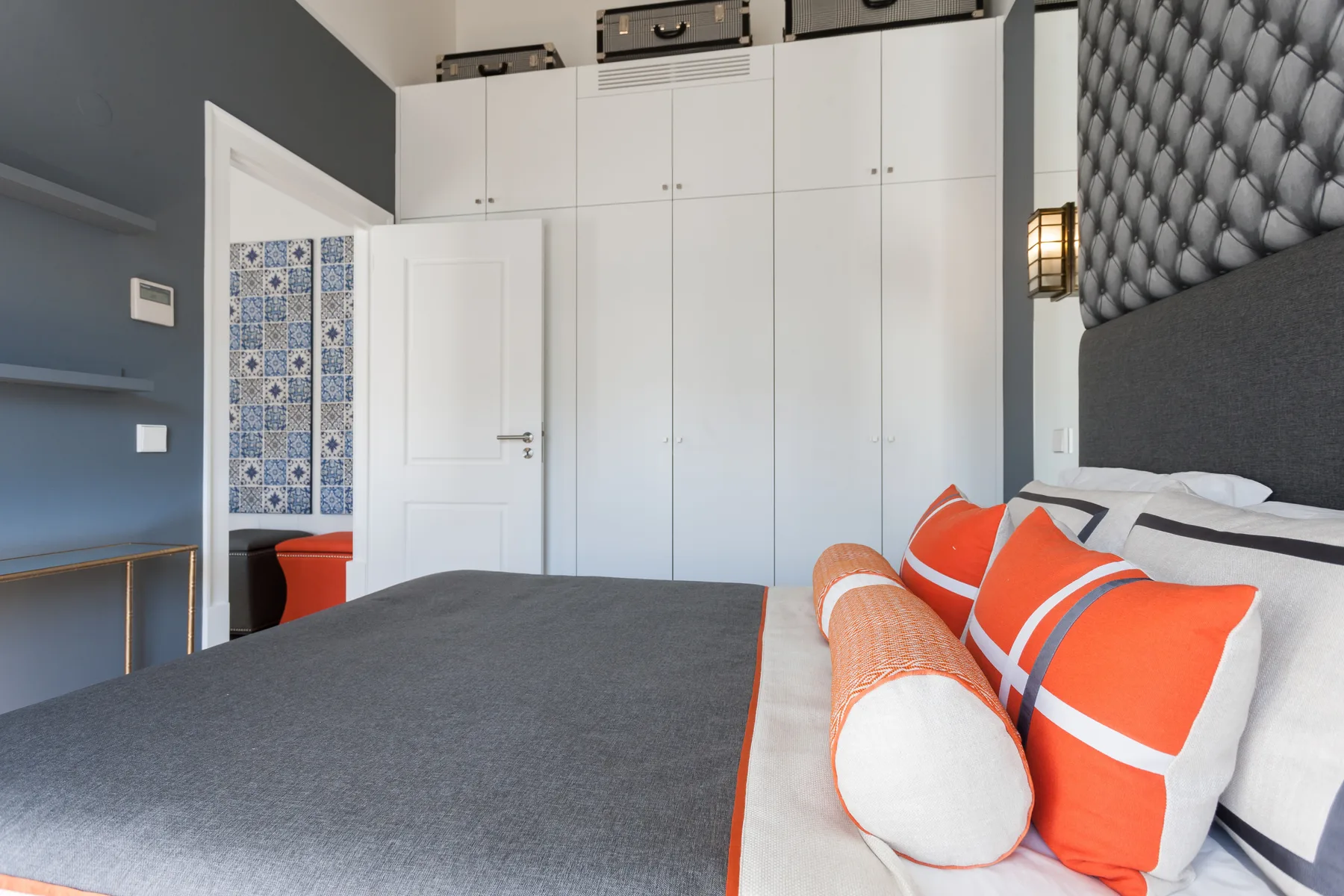 Dormitorio con una cama vestida con ropa de cama gris y naranja brillante.