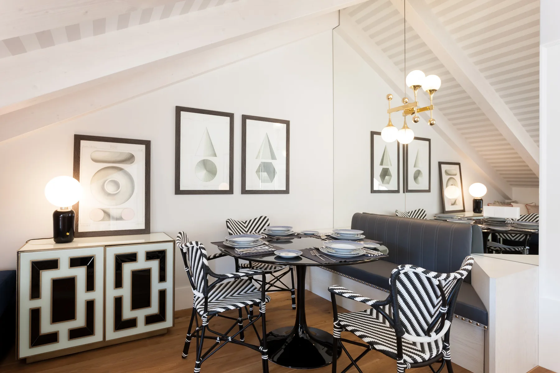 Comedor con la mesa puesta y cuadros enmarcados bajo un techo inclinado.