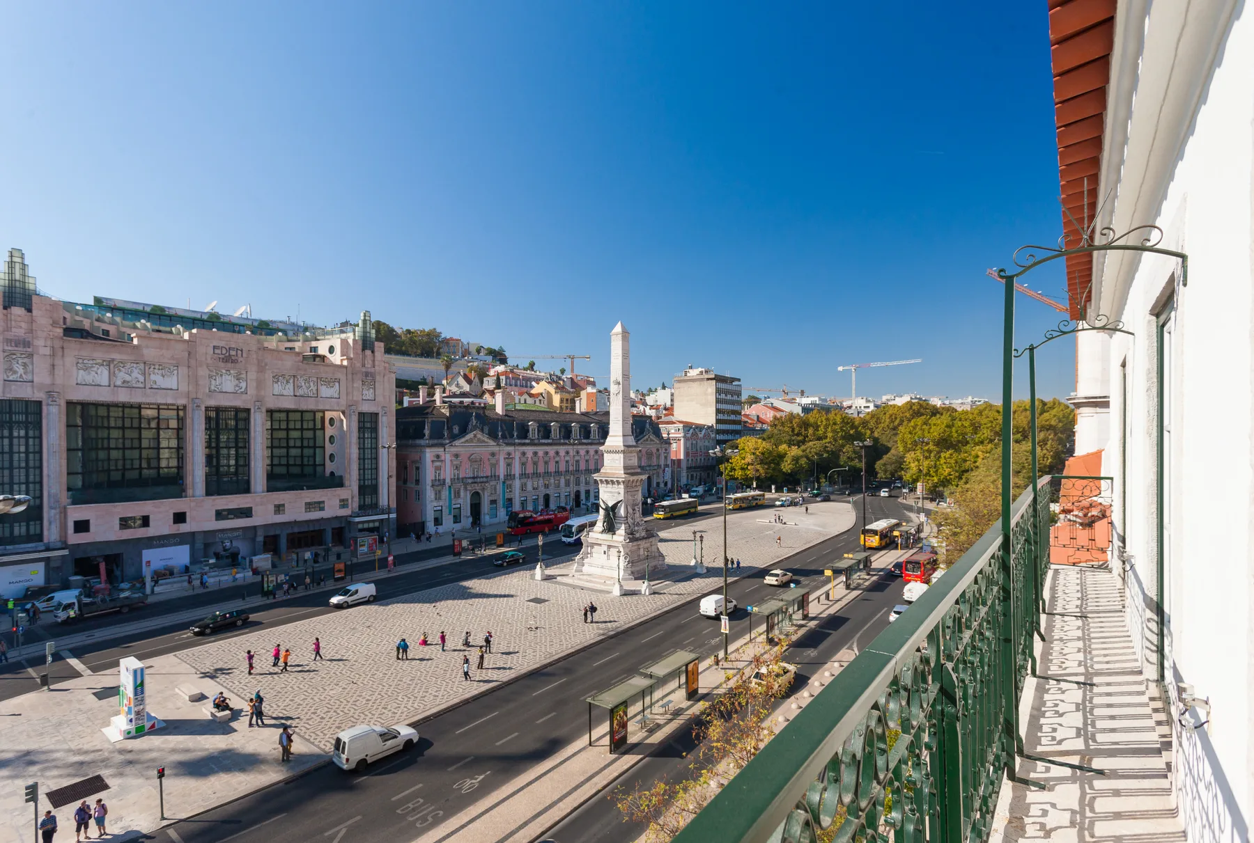 Un balcón da a una amplia plaza con un monumento y calles de la ciudad.