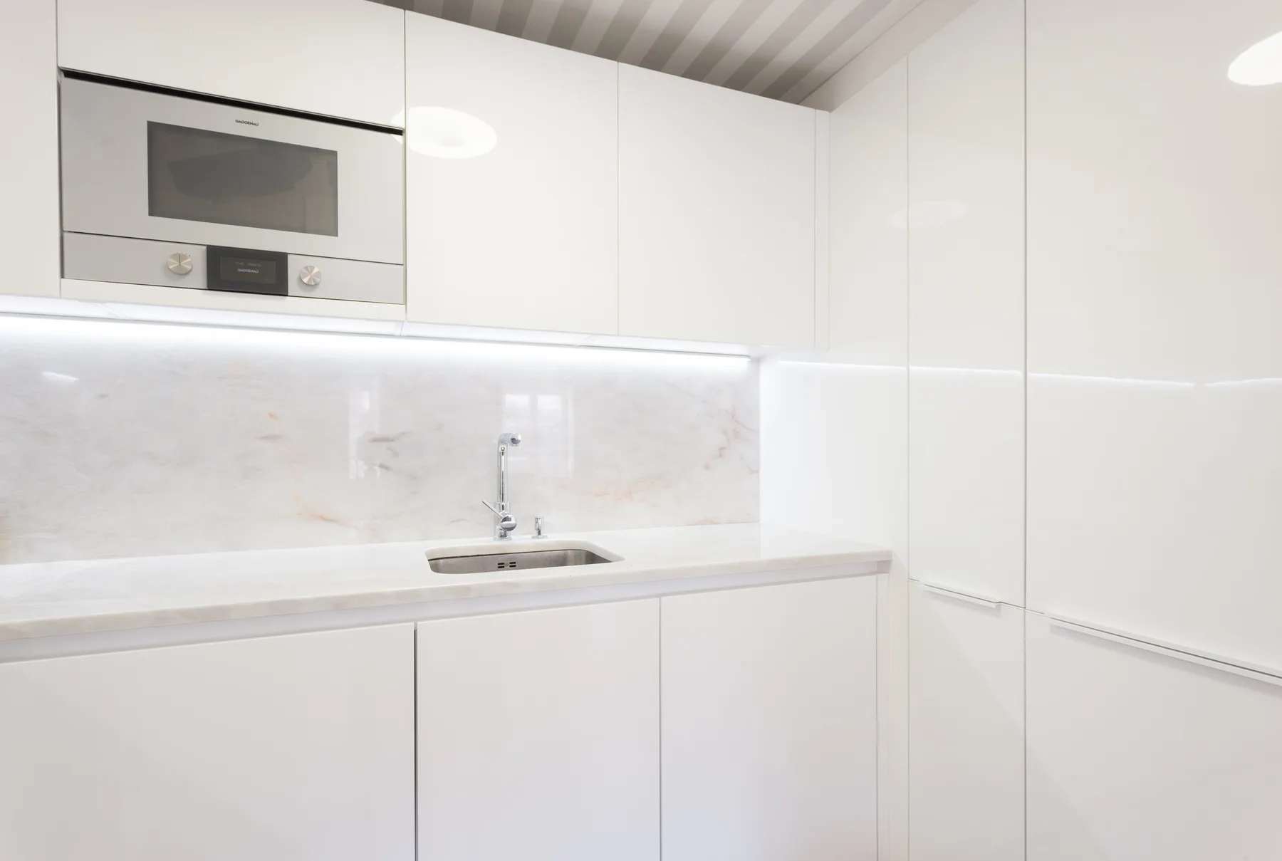 Una cocina blanca y luminosa con armarios empotrados, una encimera y un fregadero.