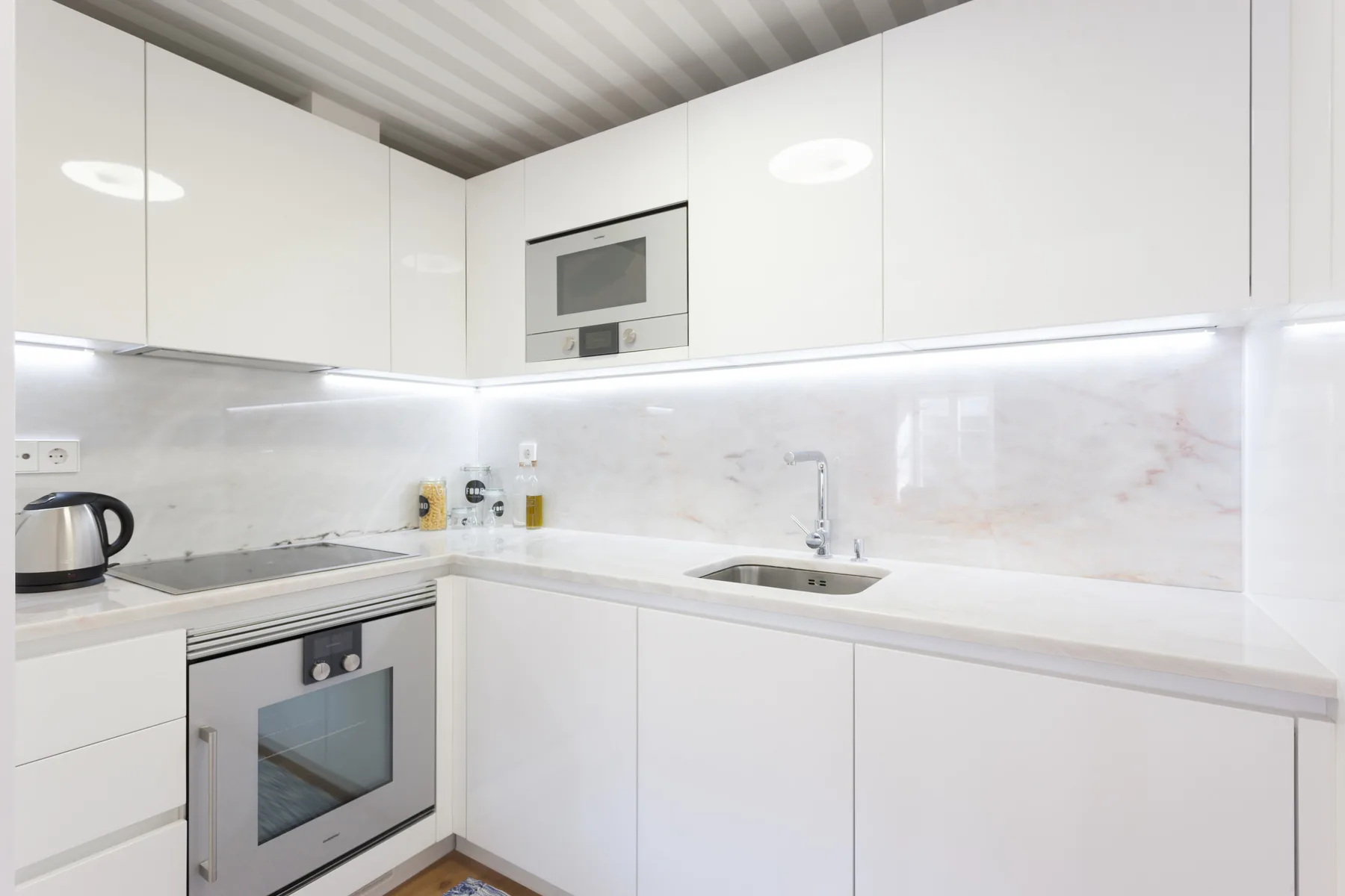 Una cocina blanca y luminosa con electrodomésticos integrados y fregadero.