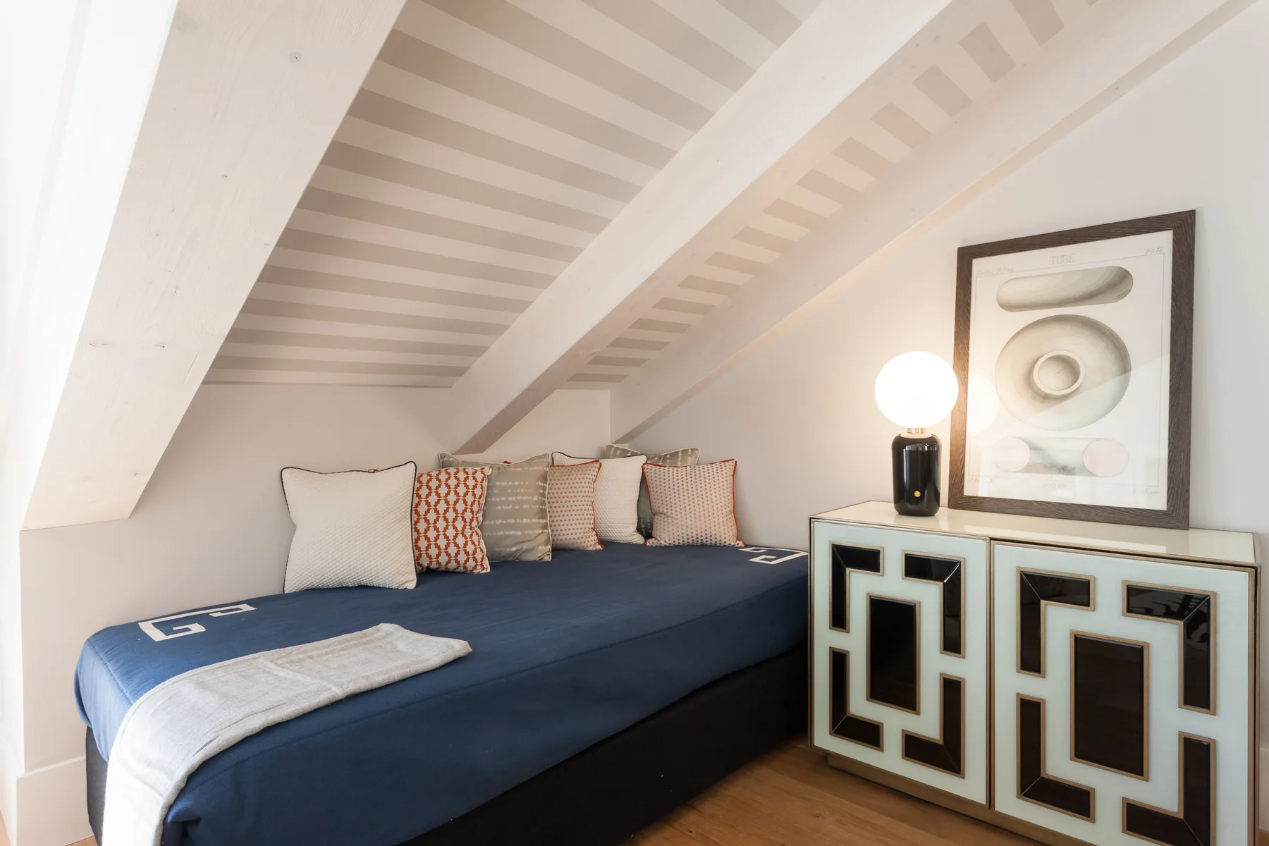 Un dormitorio con una cama baja y un mueble estampado bajo un techo inclinado.