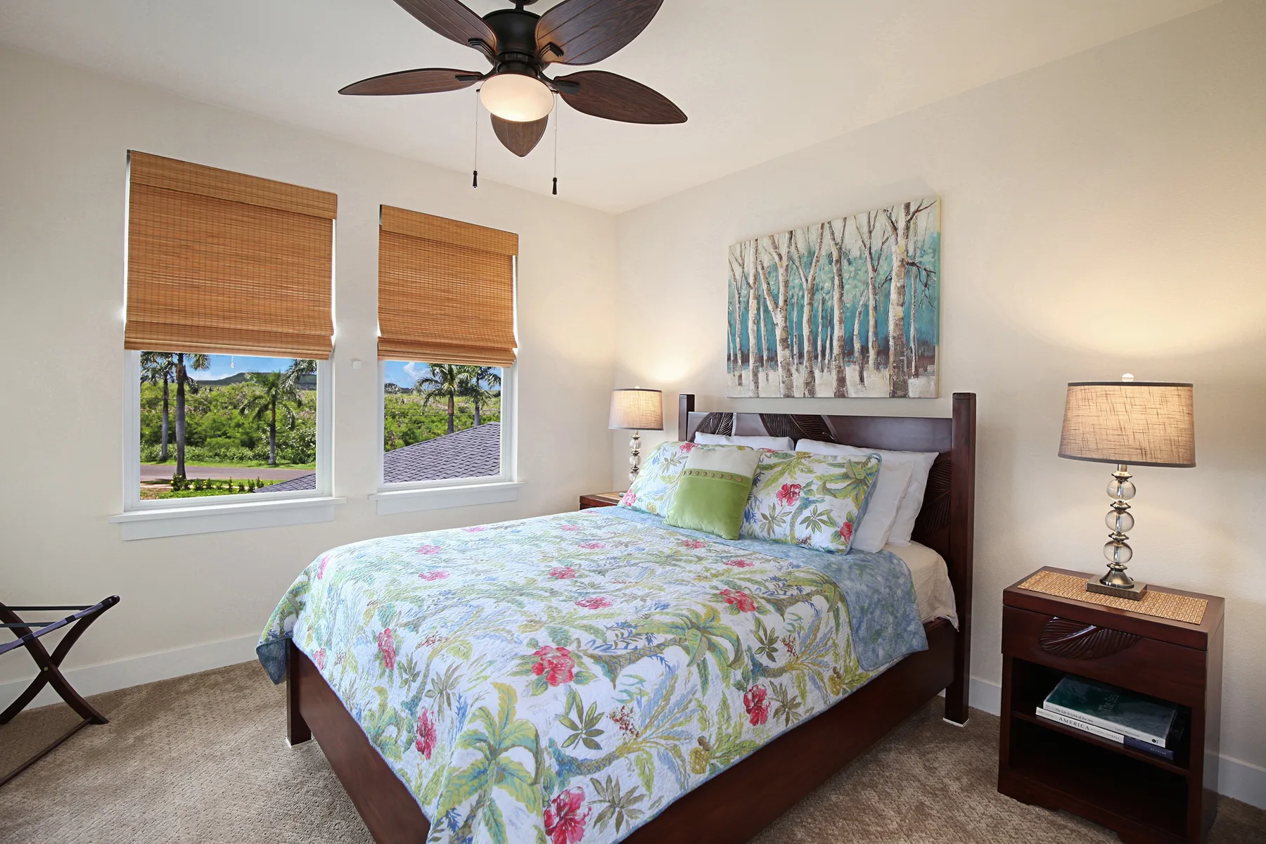 Un dormitorio con una colcha floral, mesitas de noche y ventanas con vista a la vegetación.