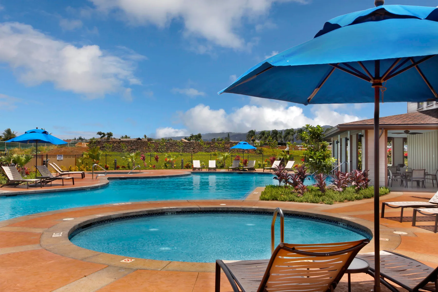 Una zona de piscina al aire libre con un spa redondo y sombrillas azules.