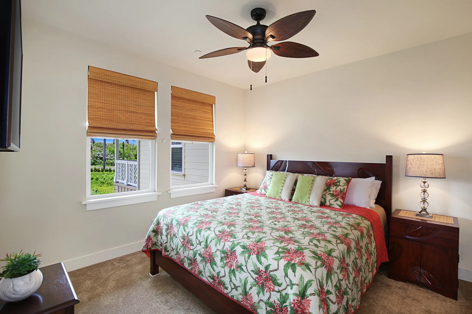 Un dormitorio con una cama grande, ropa de cama floral y ventanas con persianas tejidas.
