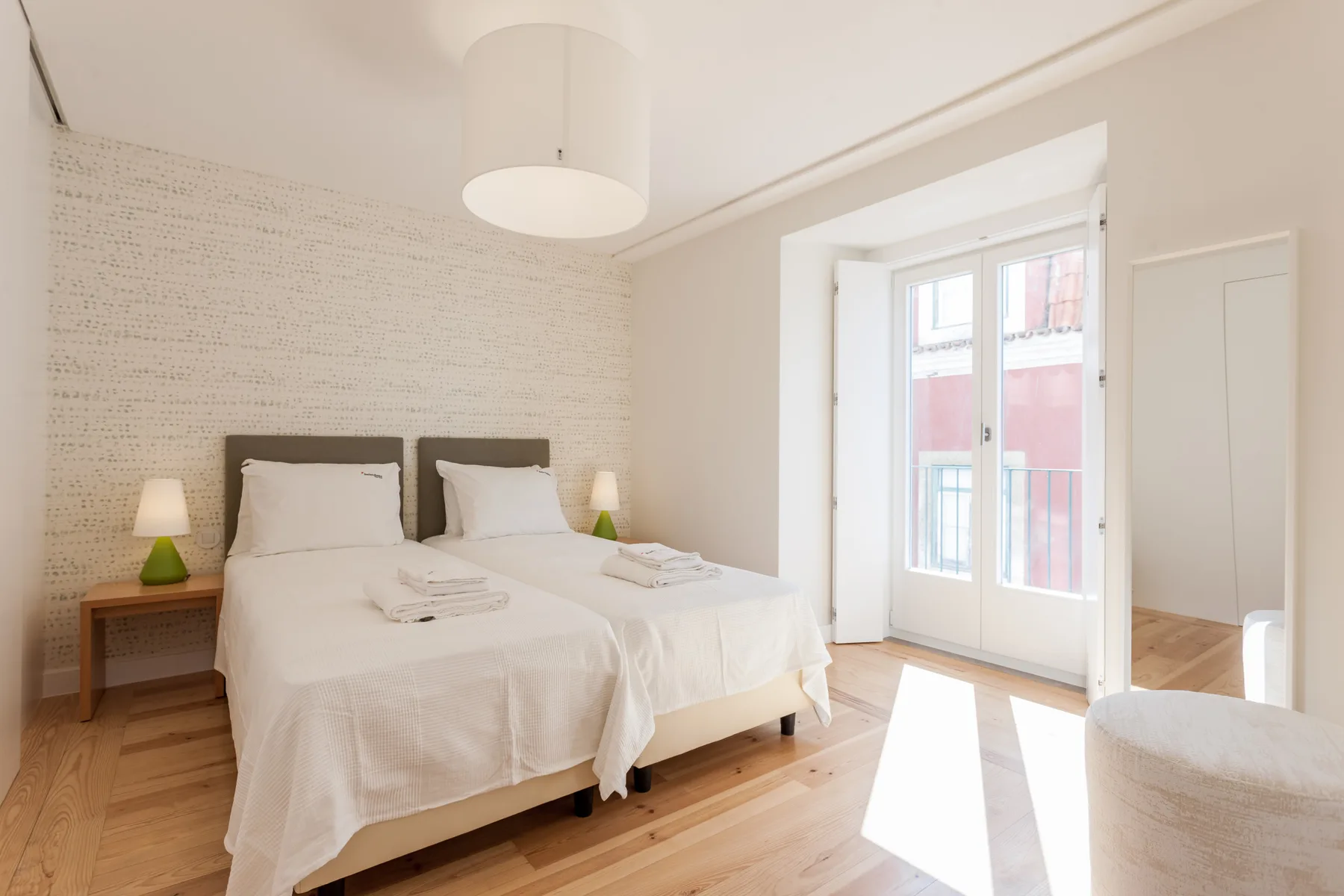 A bright bedroom with two beds beside a large window.
