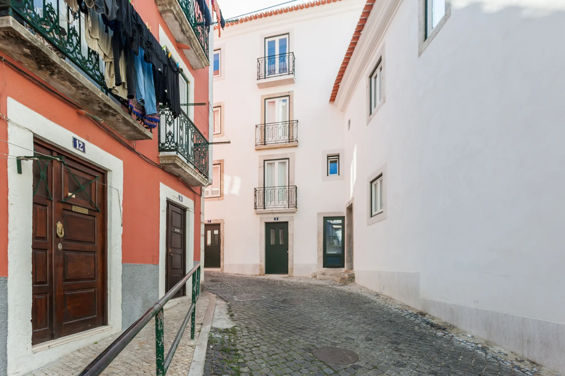 A narrow cobblestone street runs between colorful buildings with balconies.