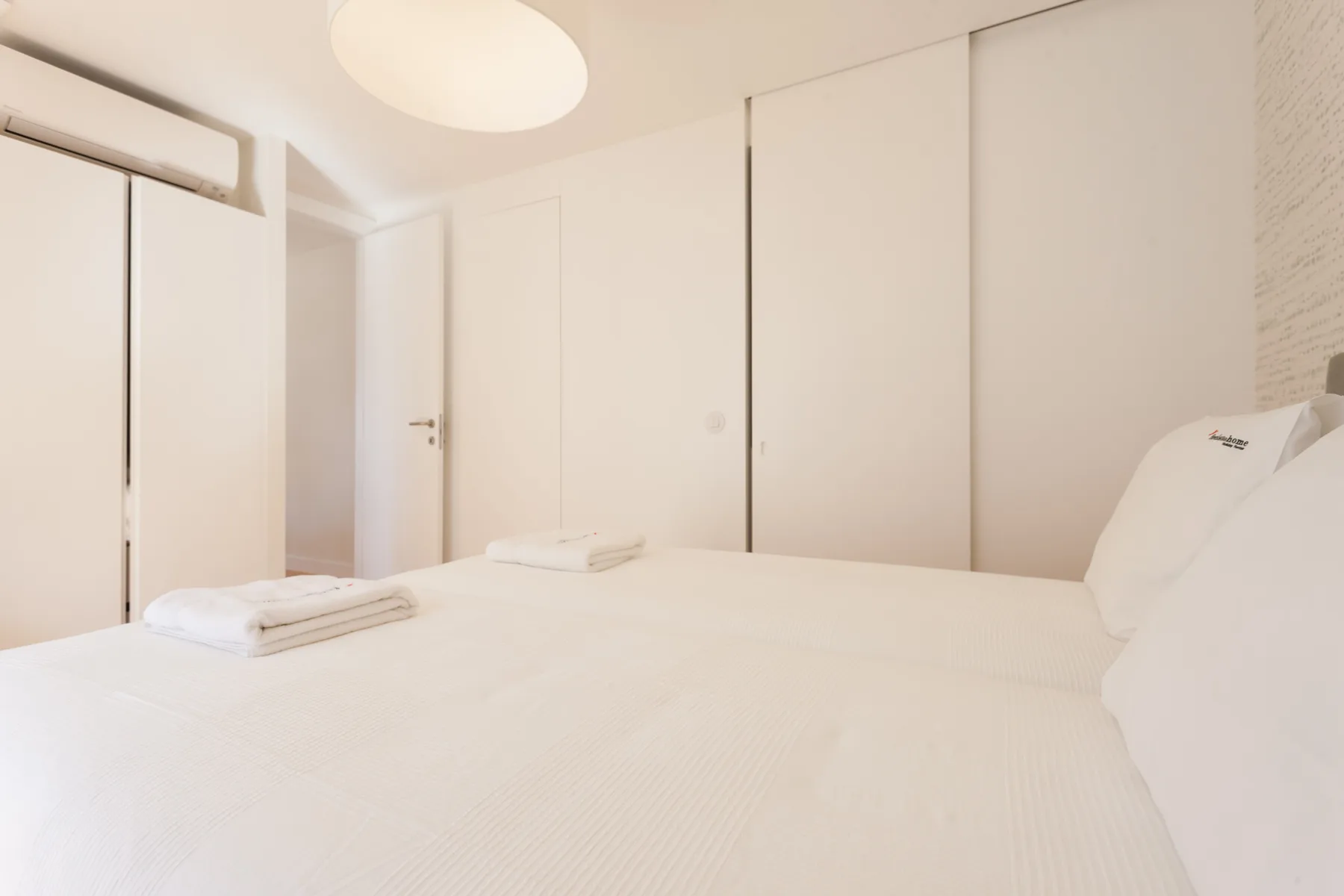 A bright bedroom with white bedding and built-in wardrobes.