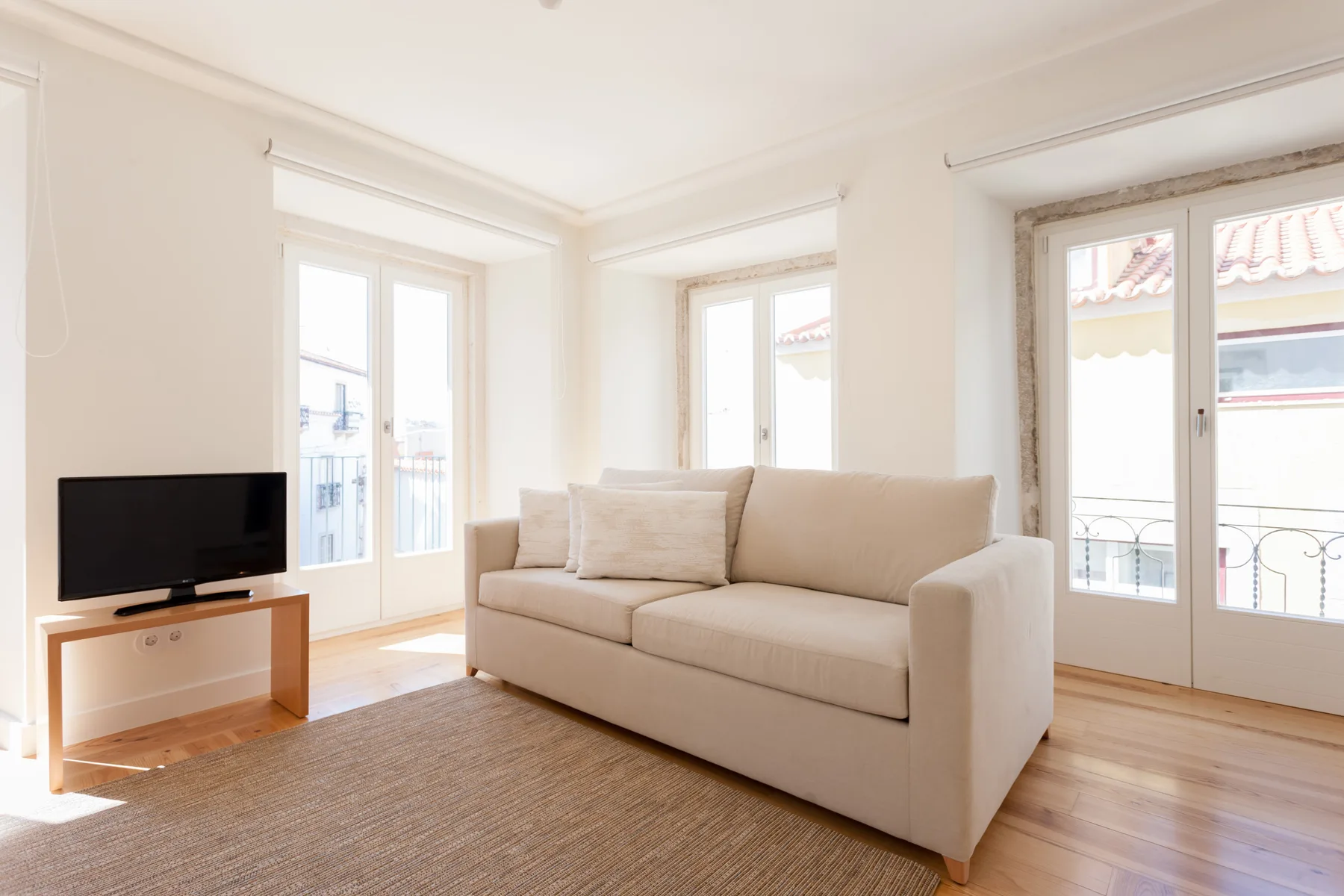 A bright living room with a sofa, television, and large windows.