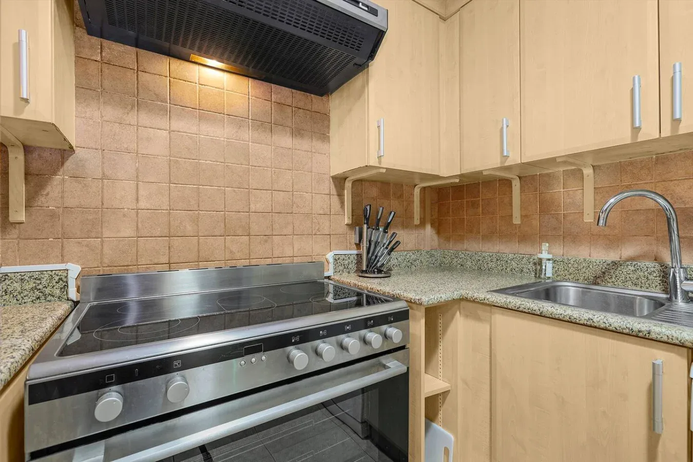 A kitchen with a stovetop, oven, sink, and light wood cabinets.