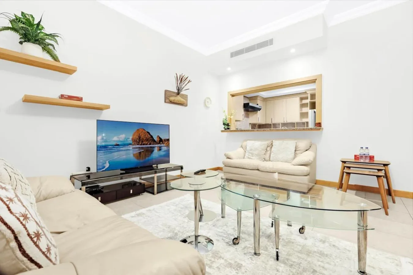 A bright living room with seating, glass tables, and a television.