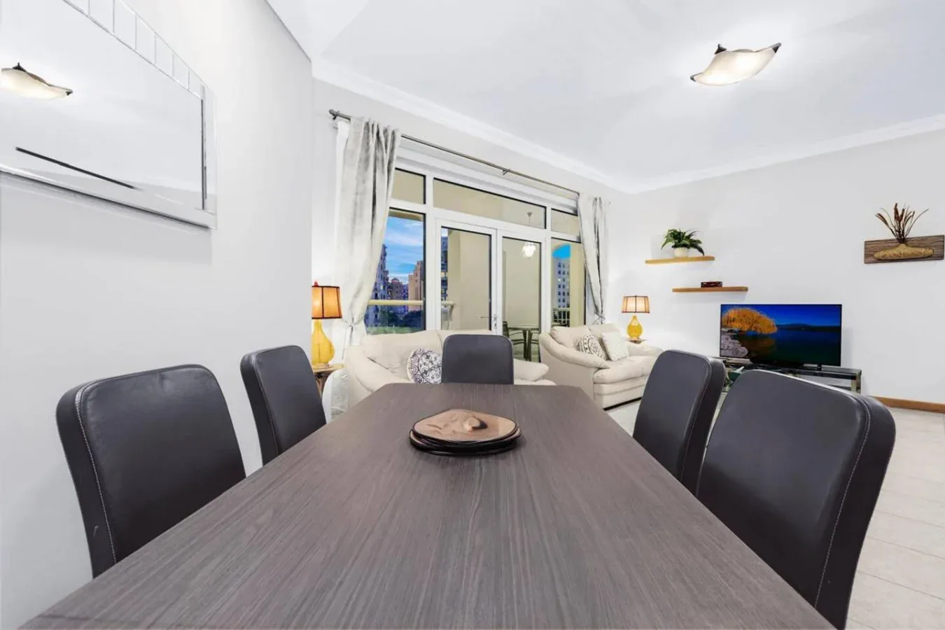 A dining area with a large table and seating, opening onto a bright living room.