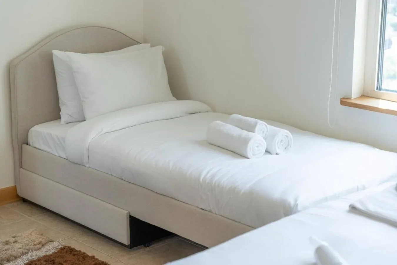 A bright bedroom with a neatly made bed and folded towels.