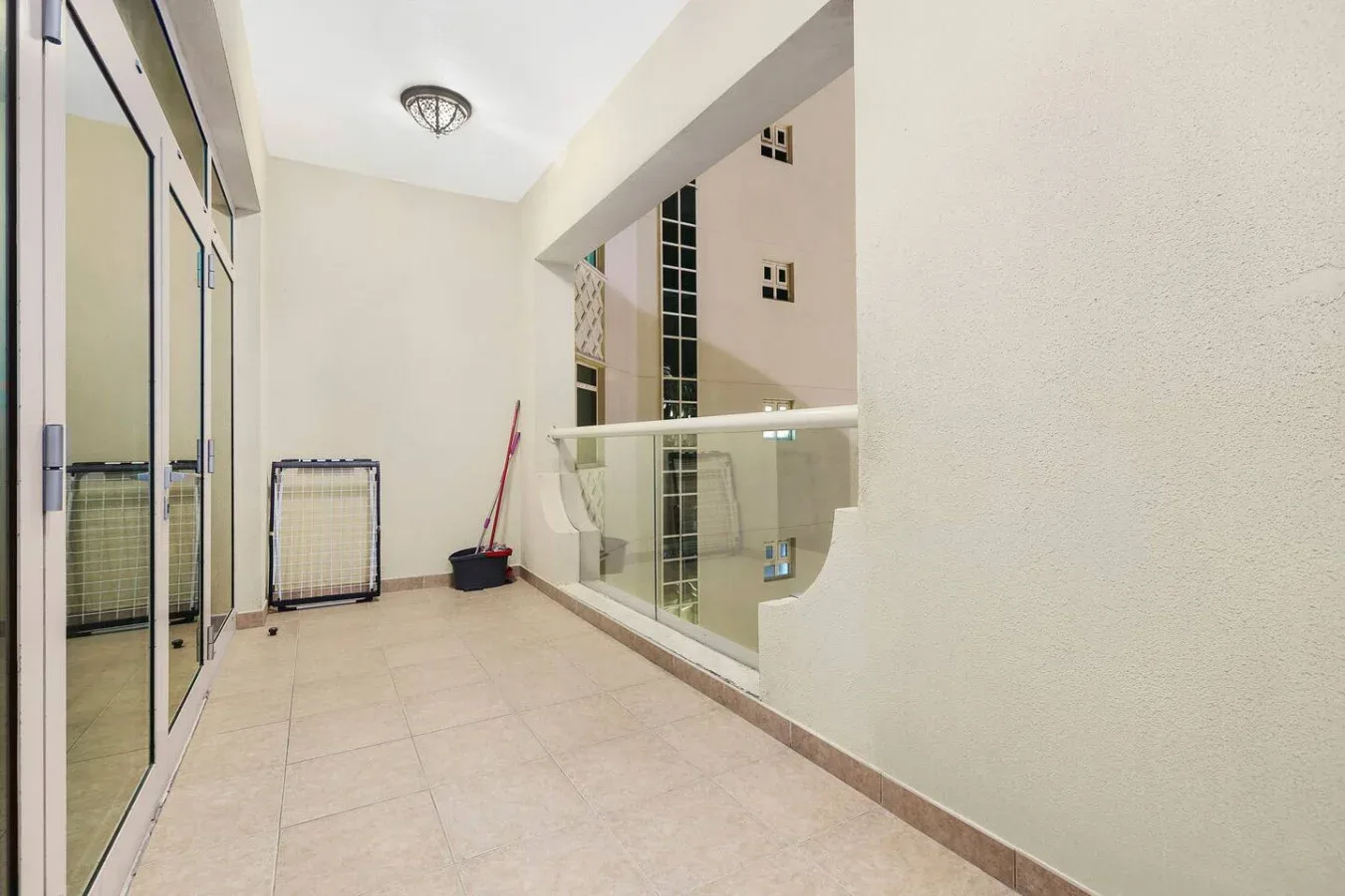 A tiled indoor hallway with a glass railing and cleaning tools near the wall.