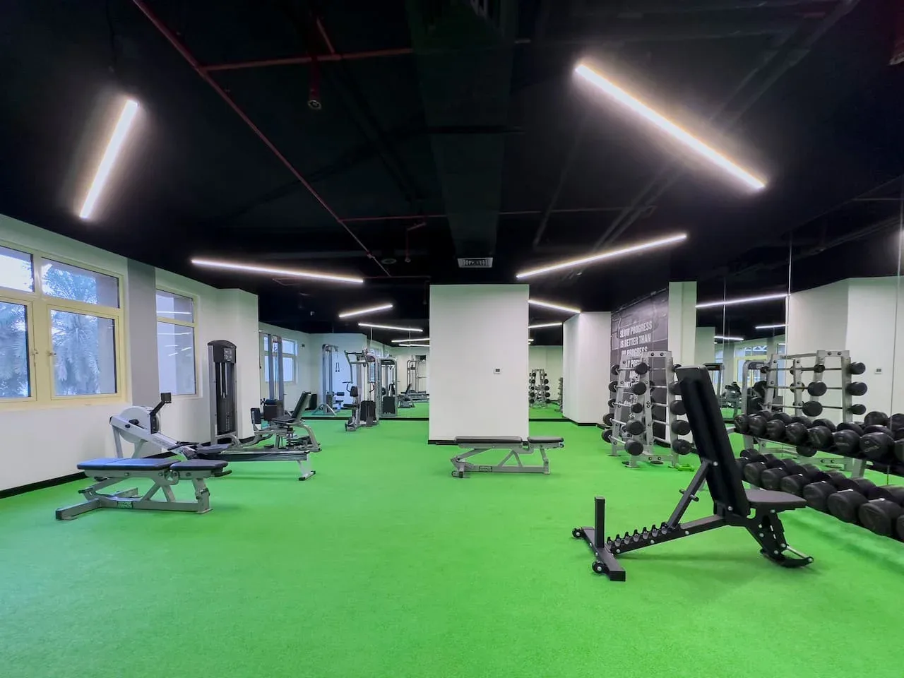 A gym with green flooring, exercise benches, and weight racks.