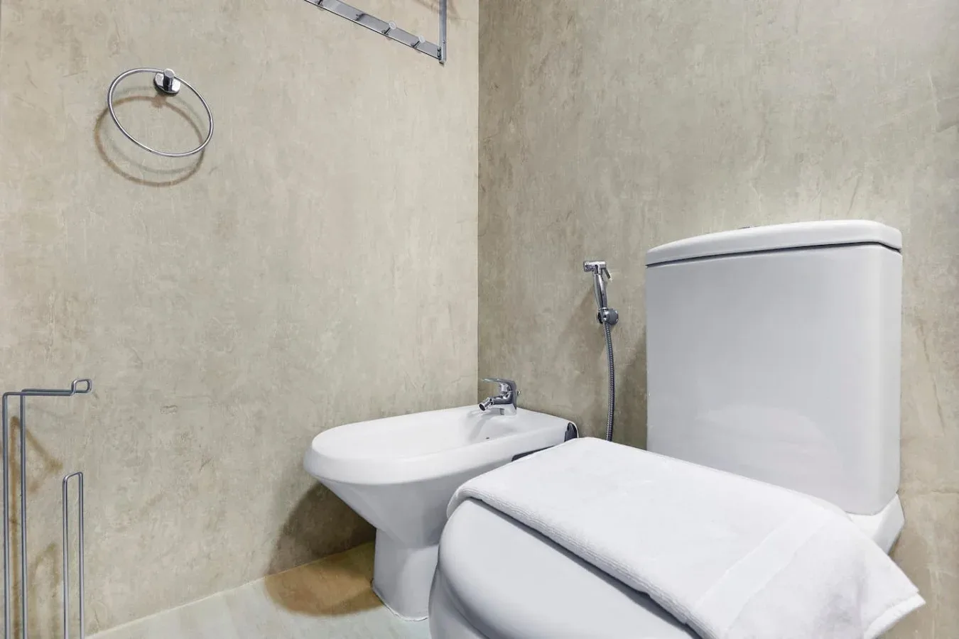 A bathroom with a bidet and toilet, with a folded towel draped over the toilet.