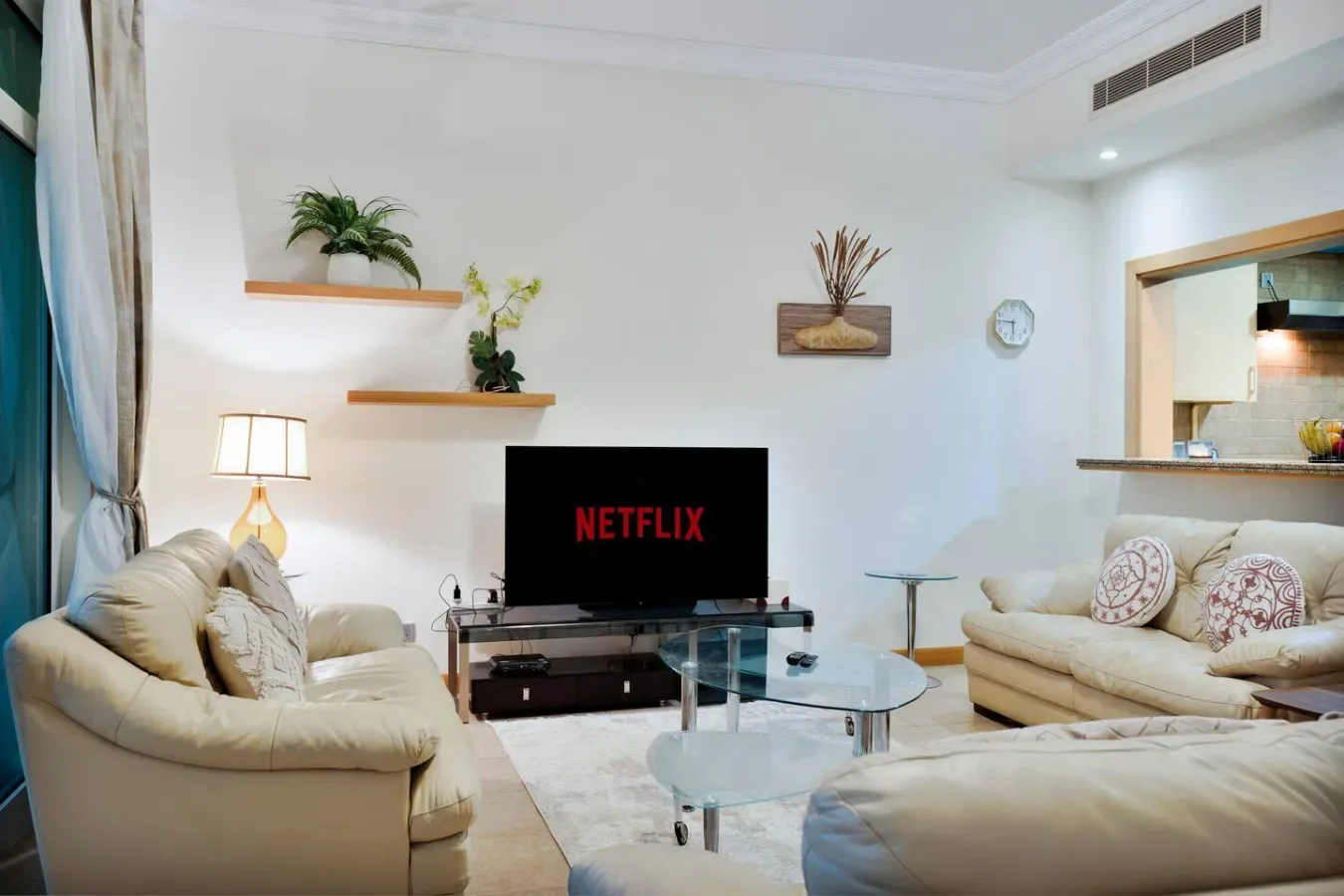 A living room with cream seating, a television, and a glass coffee table.