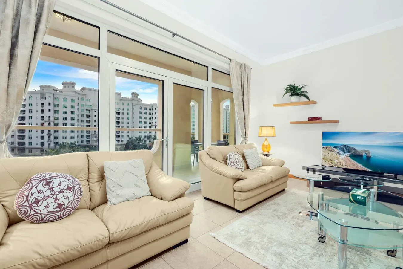 A bright living room with beige seating, large windows, and a television.